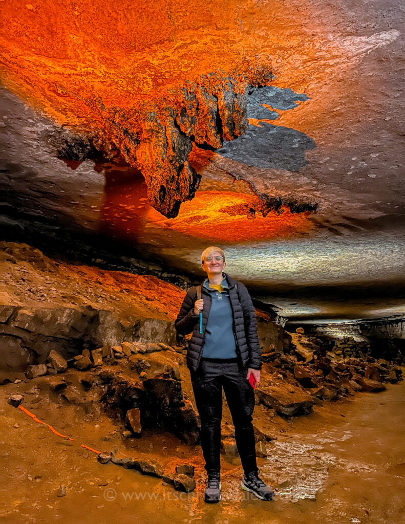 Alex standing under a stalactite illuminated orange in the Gothic Avenue of Mammoth Cave National Park 