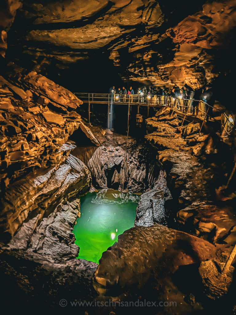 A park ranger shines a flashlight into the blue and green River Styx in Mammoth Cave National Park