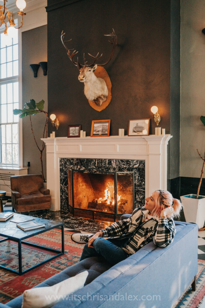 Queer woman sits on a couch near a blazing fireplace in the lobby of the Hood River Hotel in Hood River, Oregon.